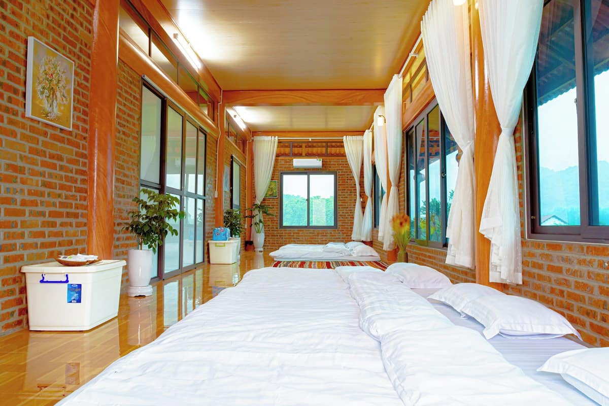 Ein Hotelzimmer mit Backsteinwand, großen Fenstern, einem Bett, einem Nachttisch und einer Zimmerpflanze.