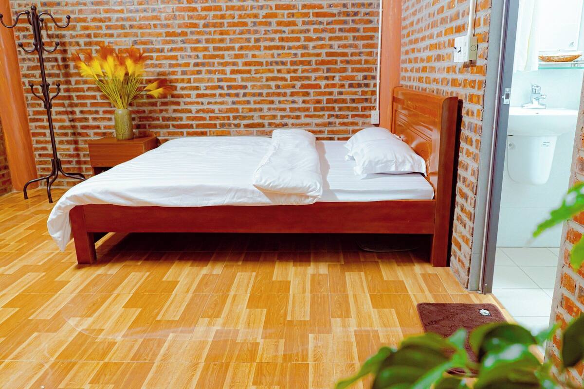 Ein ordentlich bezogenes Bett mit weißen Leinentüchern in einem Zimmer mit Backsteinwand und Holzboden.