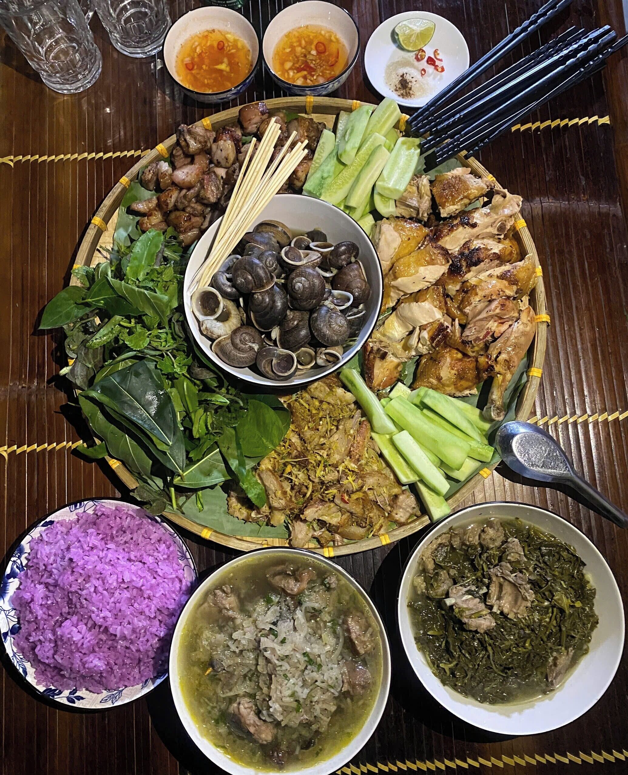 A large, round dining table with various dishes including rice, soup, and meat, surrounded by glasses and chopsticks.