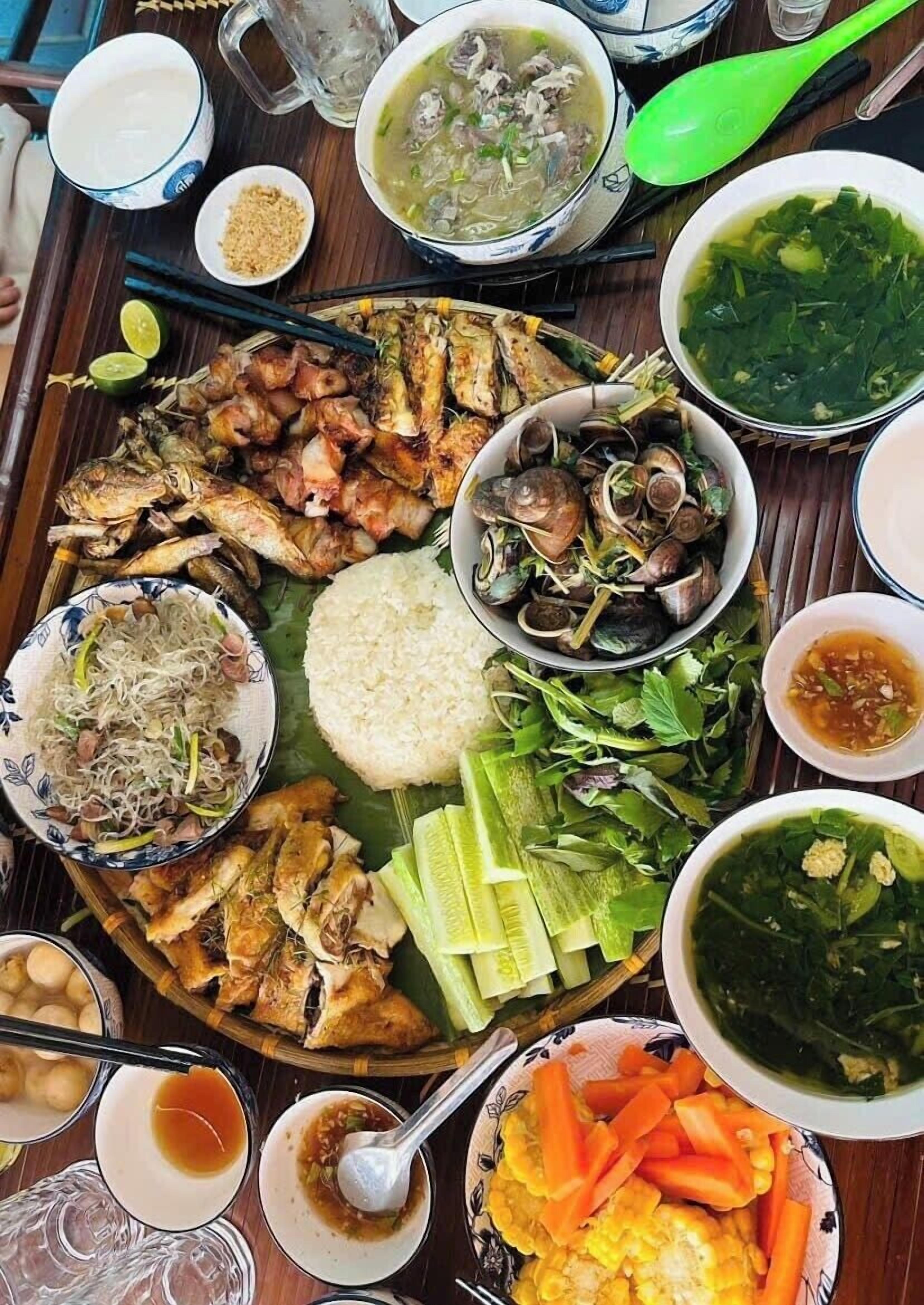 A large, round, communal dining table with various dishes, including seafood, rice, and vegetables, suggesting a shared meal setting.