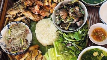 A large, round, communal dining table with various dishes, including seafood, rice, and vegetables, suggesting a shared meal setting.