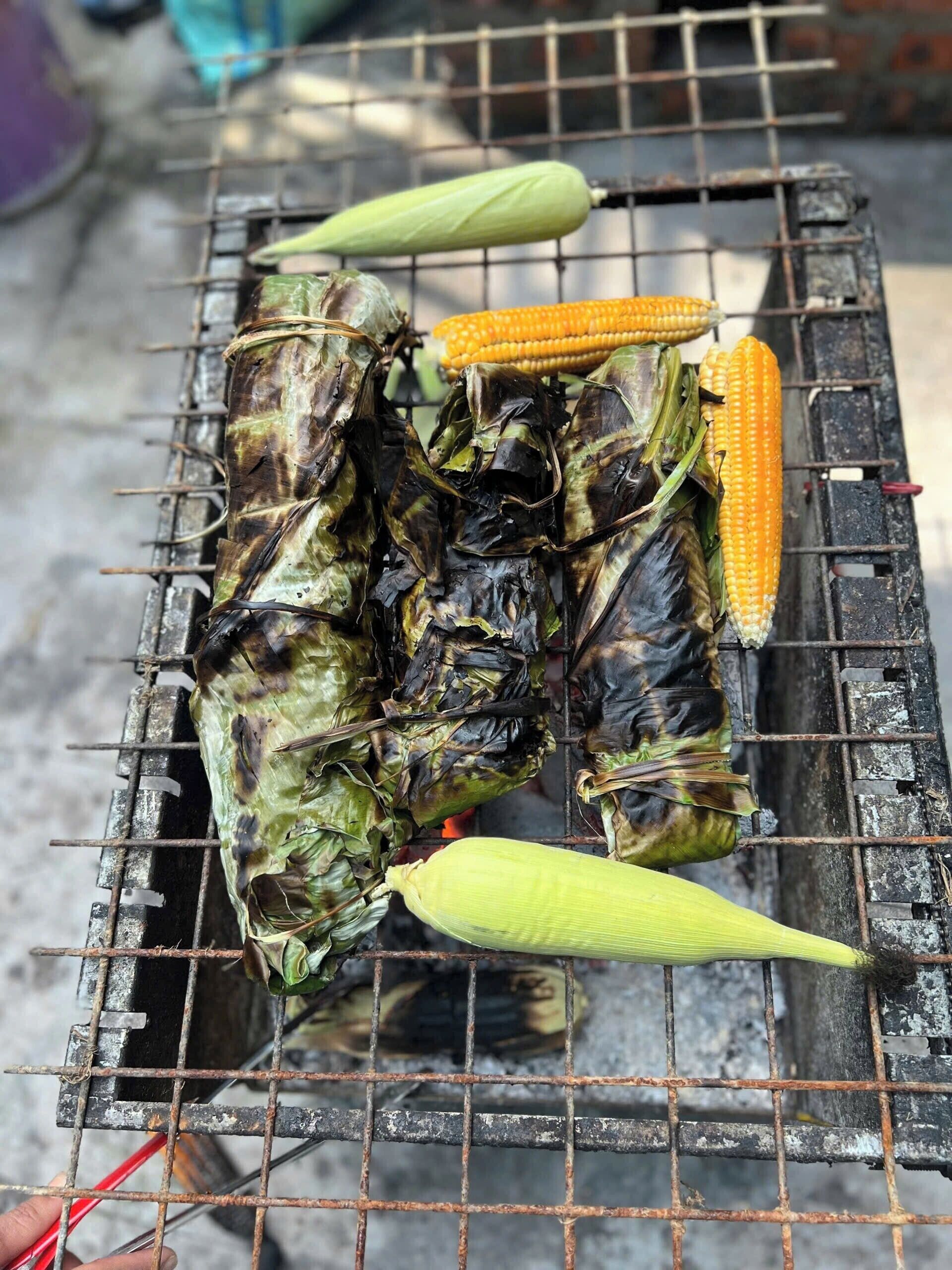 A grill with corn on the cob and tamales being cooked.