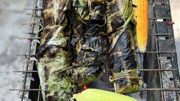 A grill with corn on the cob and tamales being cooked.