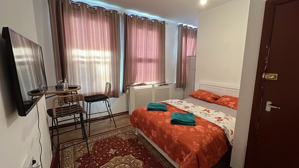 A bedroom with a bed, a desk, a chair, a radiator, and a door.