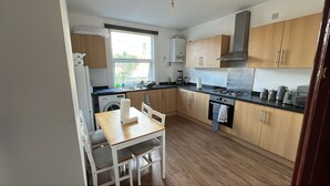 A compact kitchen with a washing machine, a dining table with chairs, a window, and wooden cabinets.
