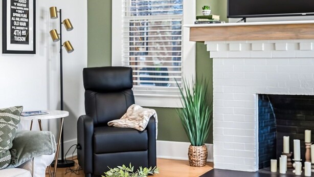 Un salon comprenant un fauteuil en cuir noir, une table basse ronde en bois, un canapé blanc, une cheminée et un téléviseur fixé au-dessus de la cheminée.
