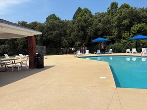 A swimming pool with lounge chairs and umbrellas, surrounded by a fence and trees.