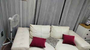 En beige soffa med två röda kuddar och en mönstrad pläd, placerad framför en grå gardin.