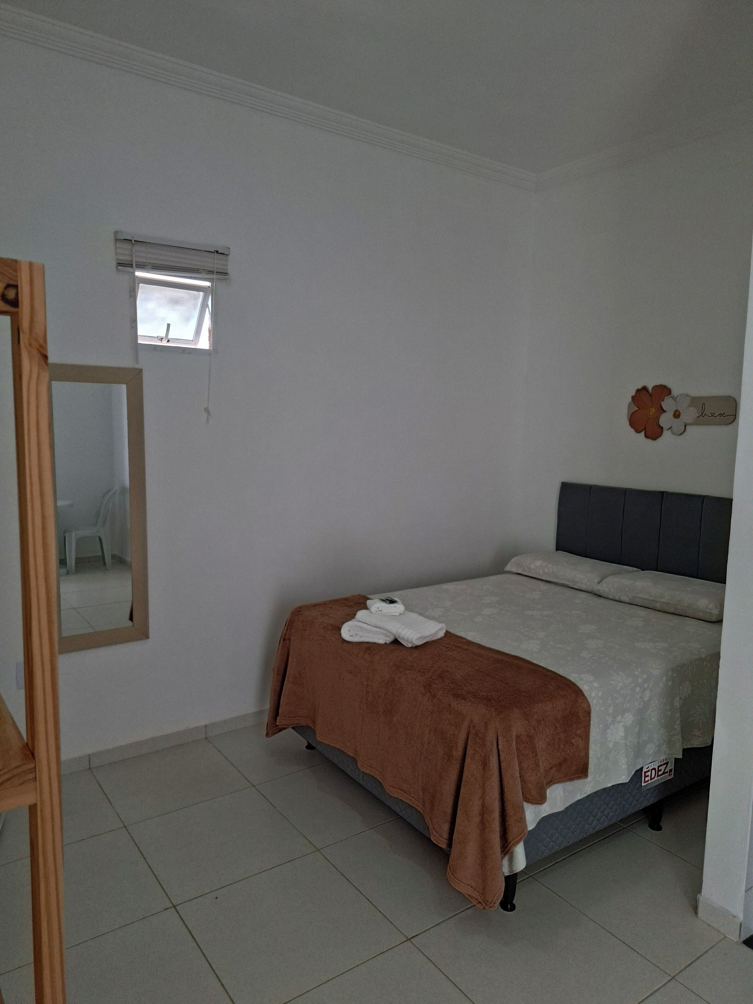 Ein Schlafzimmer mit einem Bett, einem Fenster, einem Spiegel und einer Wanddekoration.