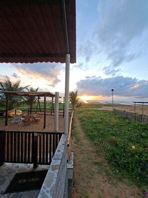 A beachside patio with a covered seating area, a wooden fence, and a view of the sunset over the ocean. - Pousada Beira Mar Suites (Maragogi)