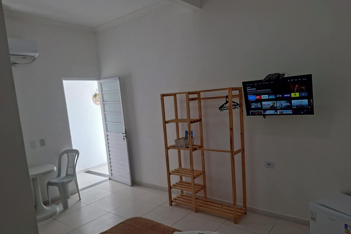 Un dormitorio con cama, un armario de madera, televisor montado en la pared y un aire acondicionado blanco.