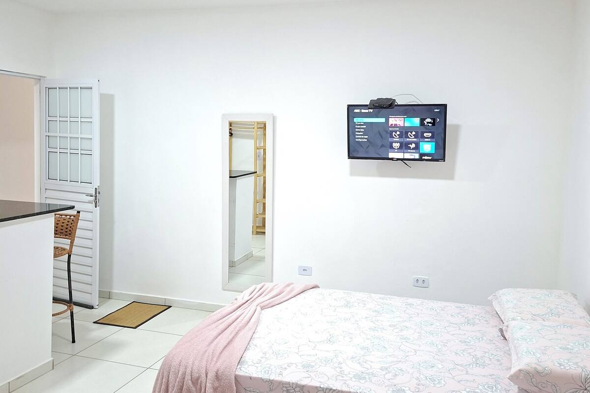 Un dormitorio con cama, escritorio, silla, televisión y puerta.
