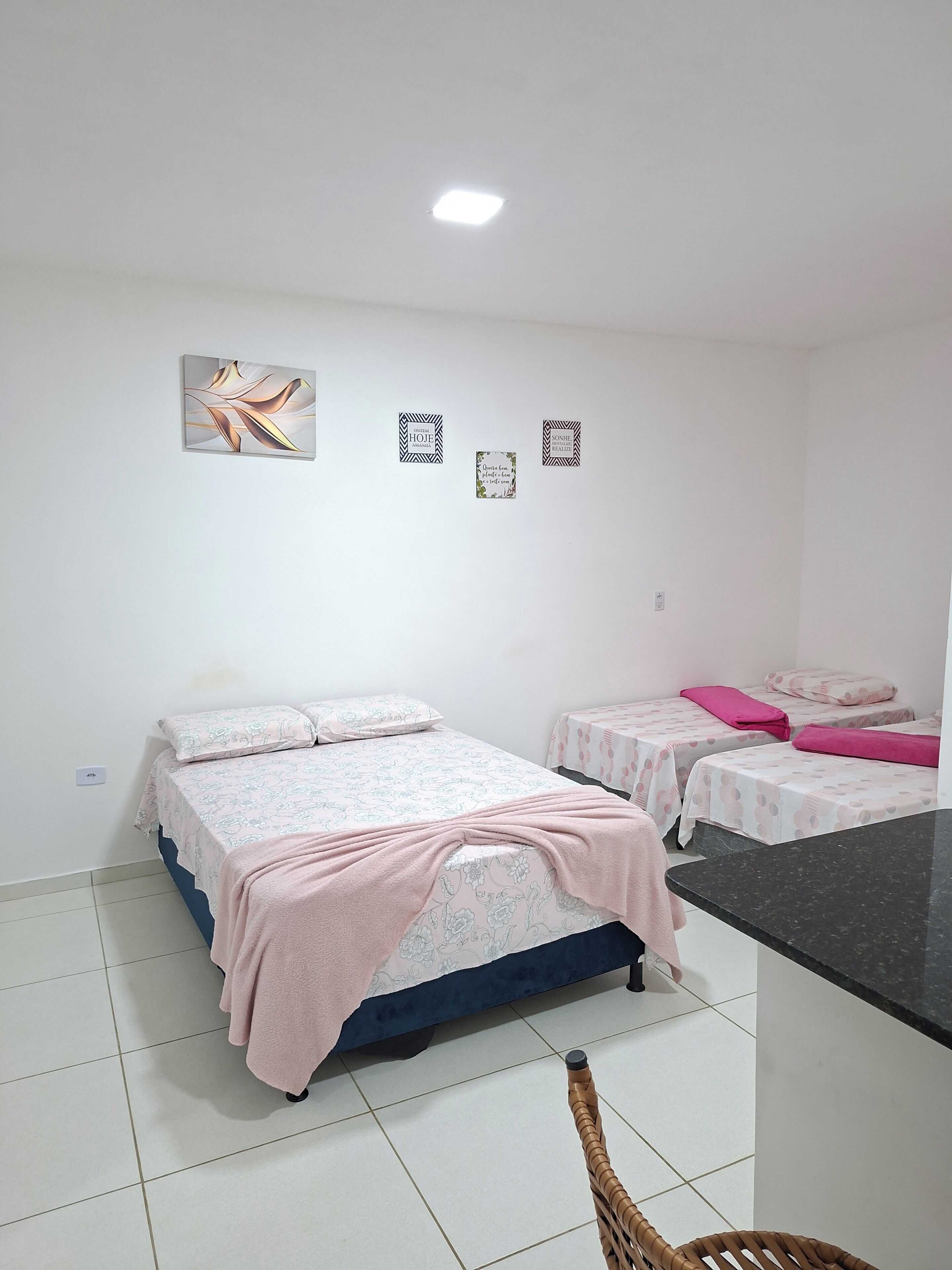 Quarto com duas camas, uma kitchenette pequena e uma cadeira.
