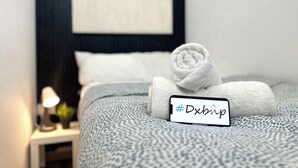 Siististi pedattu sänky, jonka päällä on rullattu valkoinen pyyhe ja kyltti, jossa on hashtag #Dxbrip.