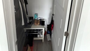 A narrow hallway with a white door on the right, a small bench with shoes and a box, and a coat rack with hanging clothes. - Spacious Downtown 1 bedroom condo with Gym, Walk to Old Port (Montréal)