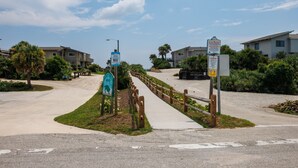 Een pad dat leidt naar een woongebied met huizen, een houten omheining en borden die een strand en een park aangeven.