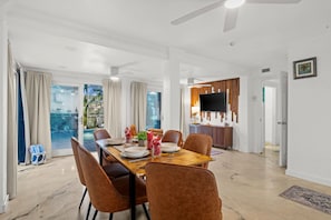 A spacious dining area with a wooden table and brown chairs, a ceiling fan, and a view of the outdoors through large windows. - Aurora Breeze Estate - The Heart of Matlacha Living (Matlacha)