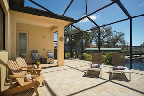 A sunlit patio with wooden chairs and a table, overlooking a pool and a clear sky. - Sunshine Pearl Residence (Cape Coral)