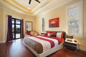 A bedroom with a large bed, a nightstand, a mirror, and a painting on the wall. - Sunshine Pearl Residence (Cape Coral)