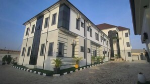 A multi-story building with a symmetrical facade, large windows, and a paved courtyard with potted plants. - Delchizz Apartment (Abuja)