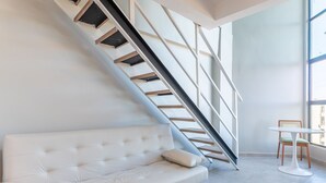 A modern interior with a white sofa, a staircase, and a small table with chairs. - Flat 1Qt na Praia dos Carneiros-SH139 (Tamandaré)