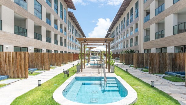 A modern building with a central pool, wooden pergola, and a fenced outdoor area. - Flat 1Qt na Praia dos Carneiros-SH139 (Tamandaré)