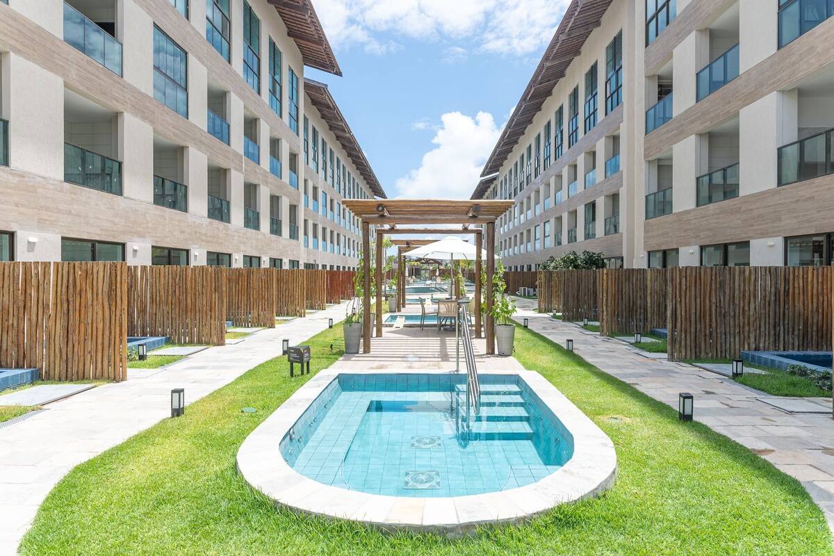 Ein modernes Gebäude mit zentralem Pool, einer Holzpergola und einem eingezäunten Außenbereich.