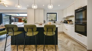 Una cocina moderna con armarios blancos, una isla central con taburetes, horno empotrado e iluminación colgante.