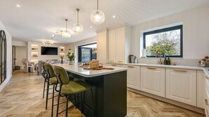 Cocina moderna con una isla central, taburetes de bar, iluminación colgante y un amplio ventanal que proporciona luz natural.