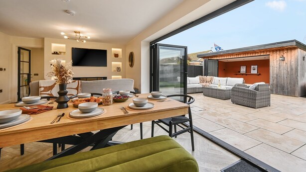 Un comedor moderno con una mesa de madera dispuesta para una comida, un sofá y un televisor montado en la pared.
