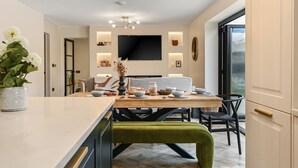 Una cocina moderna con comedor, que incluye un televisor grande, iluminación colgante y vistas al exterior.