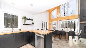 Een moderne keuken met een groot kookeiland, zwarte kastjes en een vaatwasser. Er zijn meerdere ramen en uitzicht op de omgeving.
