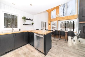 Eine moderne Küche mit einer großen Kochinsel, schwarzen Schränken und einem Geschirrspüler. Mehrere Fenster bieten einen Blick ins Freie.