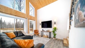 Een moderne woonkamer met een zwarte leren bank, een houten plafond en een groot raam met uitzicht op een terras.