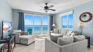 A spacious living room with a large window offering a view of the ocean, a ceiling fan, and a television on a wooden stand. - Majestic Sun B614*Gulf Views*Heated Pools/Hot Tubs*Beach Gear*Gym*Pickleball (Miramar Beach)