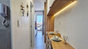 A narrow hallway leading to a dining area with a wooden table set for two, a telephone, and wall-mounted decorations. - COSTE0110 - Concept Life Stella (Salvador)