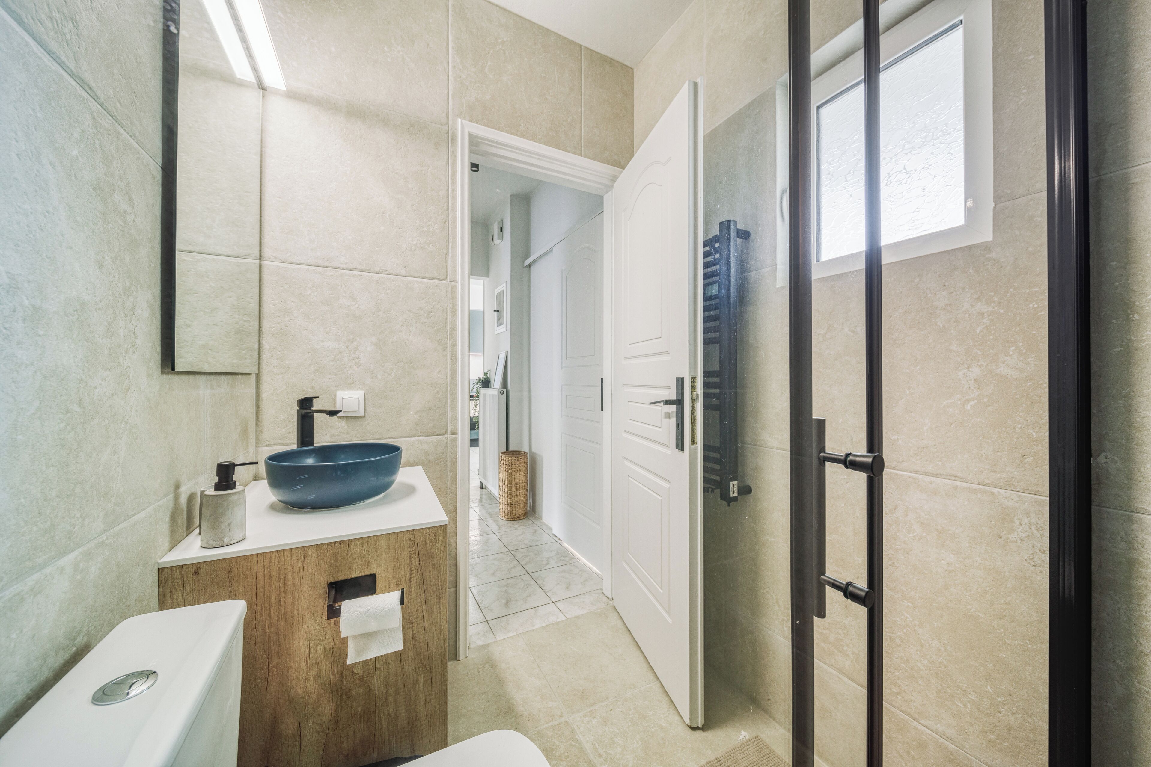 A modern bathroom with a large mirror, a wooden vanity, a blue basin, and a glass shower enclosure.