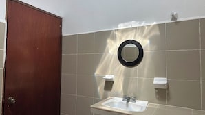 A bathroom with a wooden door, a sink, a mirror, and two towel dispensers.
