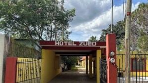A hotel entrance with a red and yellow facade, a gated driveway, and a clear sky.
