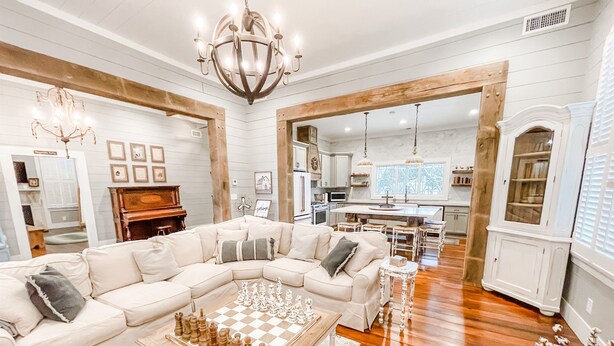 Un salon spacieux avec un grand canapé d’angle, une table basse en bois sur laquelle est posé un jeu d’échecs, et un lustre.