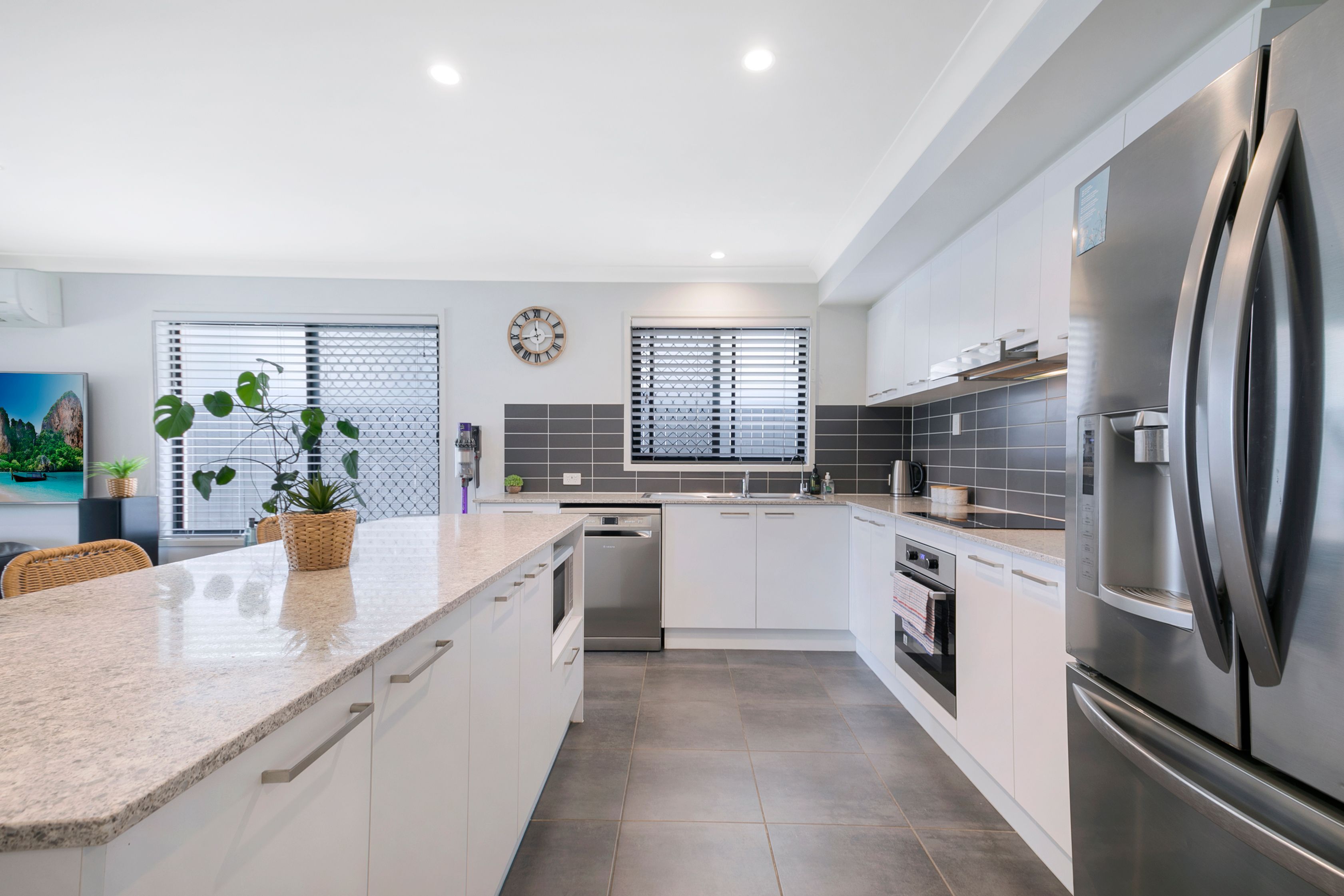 A modern kitchen with white cabinetry, a stainless steel refrigerator, and a built-in dishwasher.