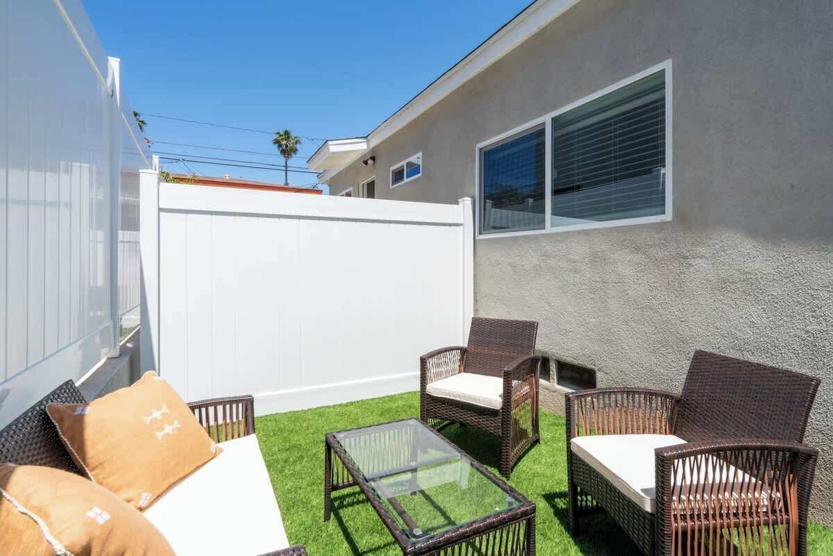 Eine Terrasse mit Korbmöbeln, einem Glastisch und einem weißen Zaun.