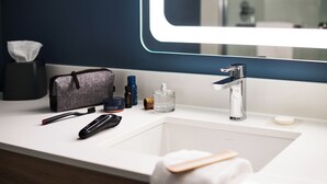 Un baño moderno con un lavamanos blanco, un espejo, una toalla, un cepillo de dientes, un afeitador y una pequeña bolsa.