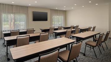 A conference room with multiple tables and chairs, large windows with curtains, and a flat-screen TV mounted on the wall.