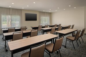 Une salle de conférence dotée de plusieurs tables et chaises, de grandes fenêtres avec des rideaux et d’un téléviseur à écran plat fixé au mur.