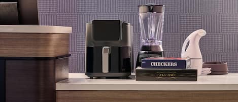 A kitchen counter with a coffee maker, a blender, a book titled 'CHECKERS,' and a water bottle.