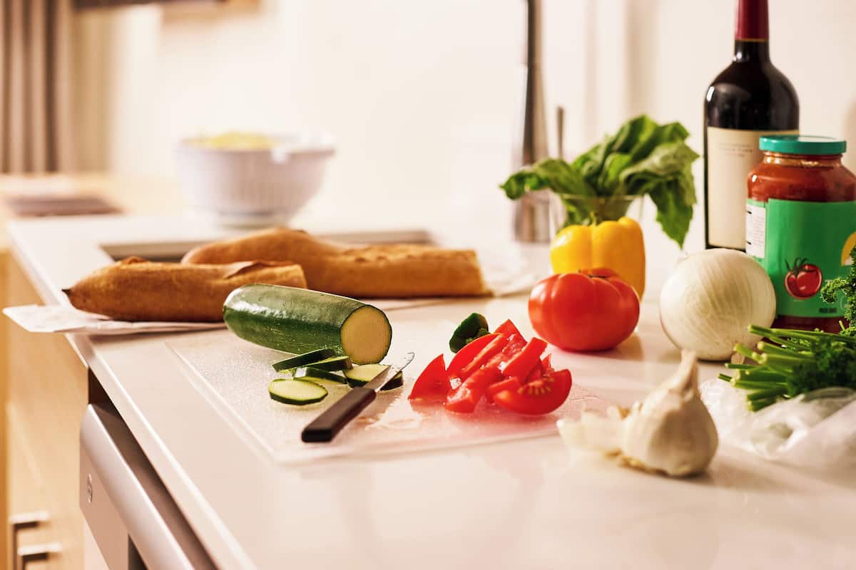 A kitchen counter with vegetables, a bottle of wine, and a jar of sauce.