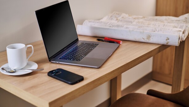 A laptop on a wooden desk with a white mug, a spoon, and a smartphone.