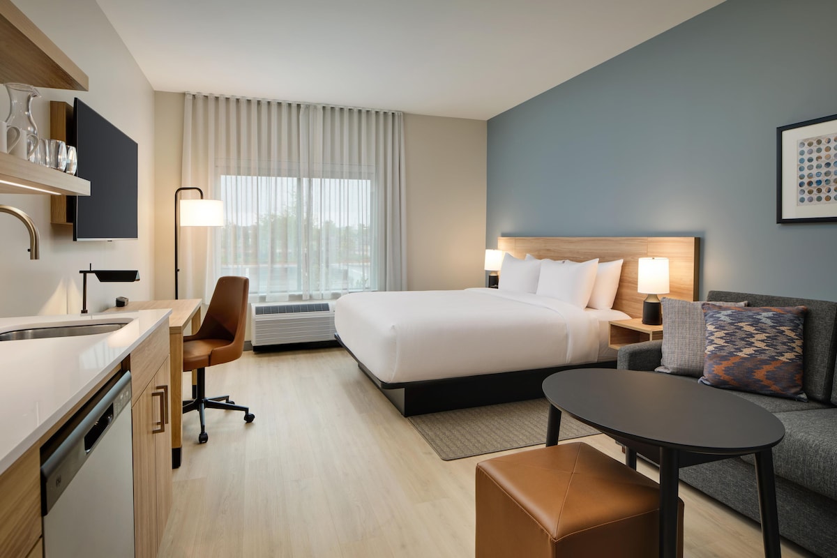 Een hotelkamer met een bed, een bureau, een stoel, een bank, een klein tafeltje en een raam met gordijnen.