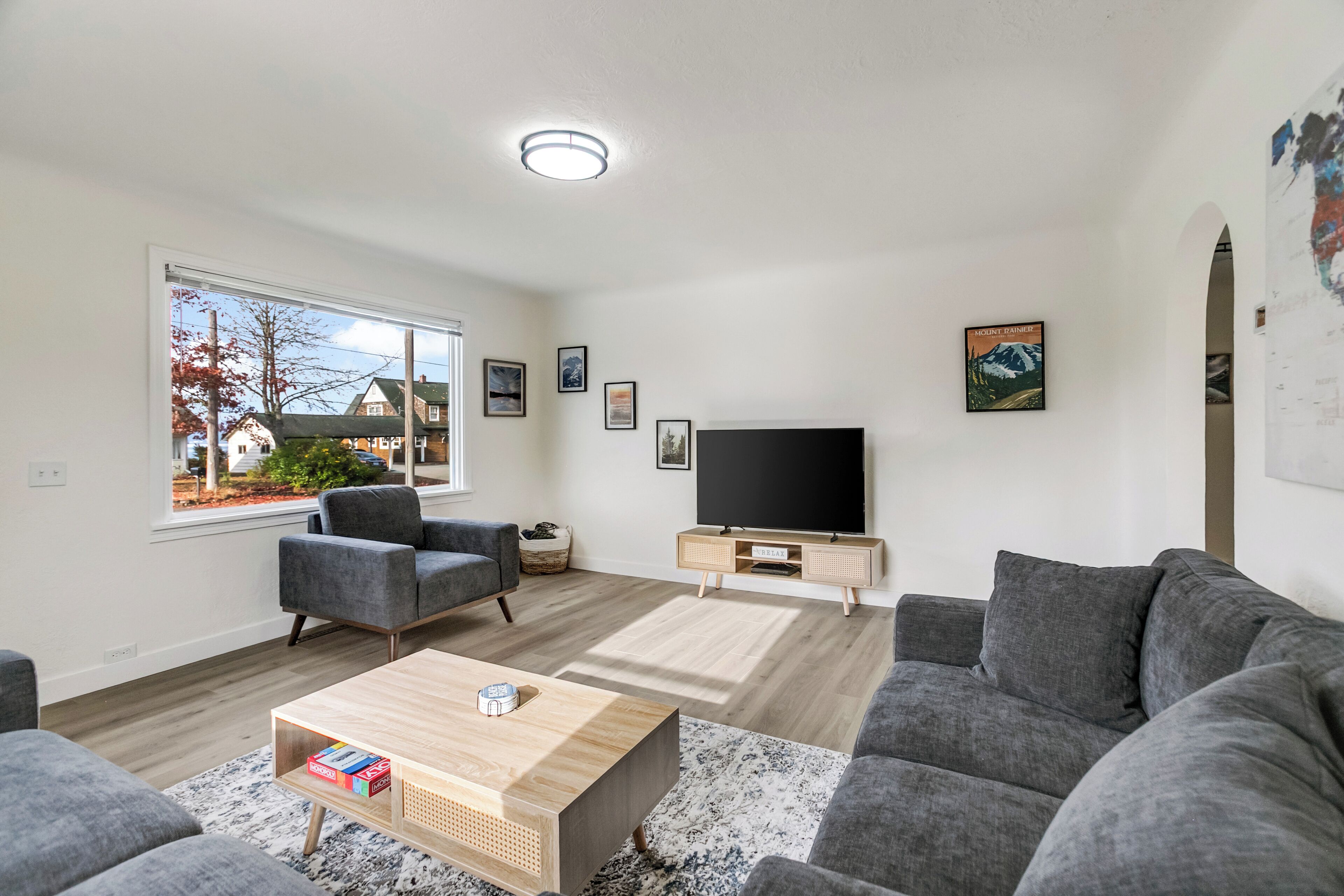A modern living room with a large window, grey sofas, a wooden coffee table, and a flat-screen TV.